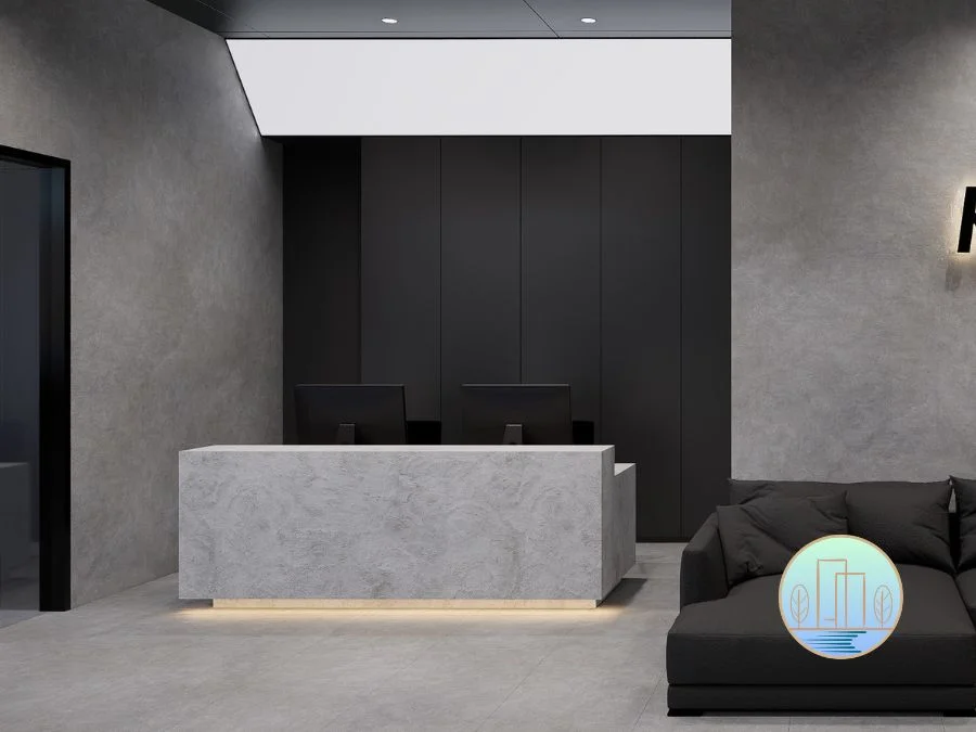 Modern office reception area featuring a light gray concrete reception desk with underlighting, dark gray textured walls, and a black sectional sofa.